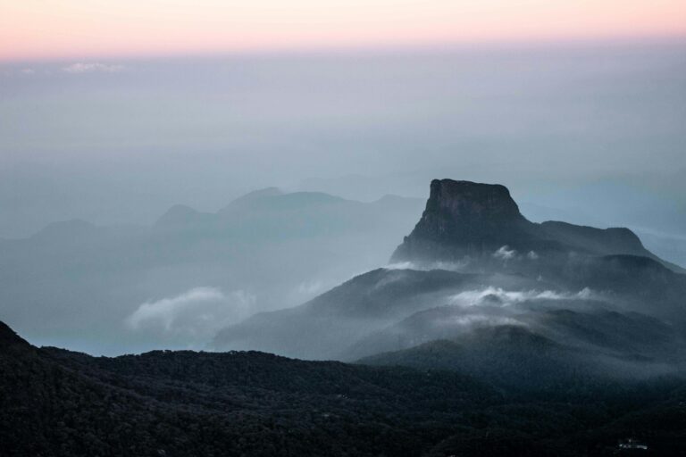 Serene view of Adam's Peak at dawn, shrouded in mist and gentle clouds, in Sri Lanka's lush landscape.